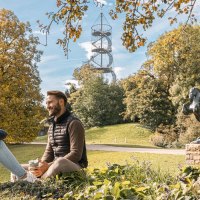 Zwei Personen sitzen im Höhenpark Killesberg, umgeben von Herbstbäumen. Im Hintergrund ist der Killesbergturm zu sehen, neben einer Pferdestatue., © Stuttgart-Marketing GmbH, Sarah Schmid