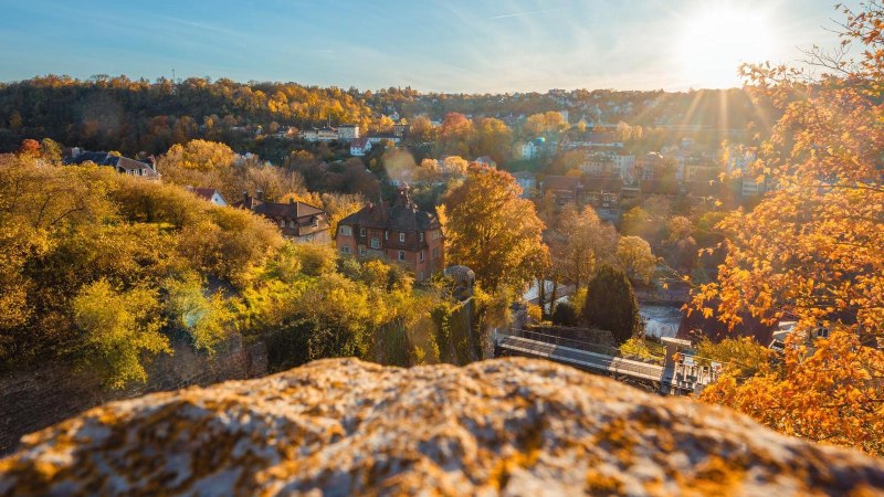Herbstliche Landschaft in Schwäbisch Hall mit buntem Laub und Sonnenstrahlen. Im Vordergrund ein Felsen, im Hintergrund Häuser und Hügel., © Stadt Schwäbisch Hall, Michael Kühneisen Herbstliche Landschaft in Schwäbisch Hall mit buntem Laub und Sonnenstrahlen. Im Vordergrund ein Felsen, im Hintergrund Häuser und Hügel., © Stadt Schwäbisch Hall, Michael Kühneisen