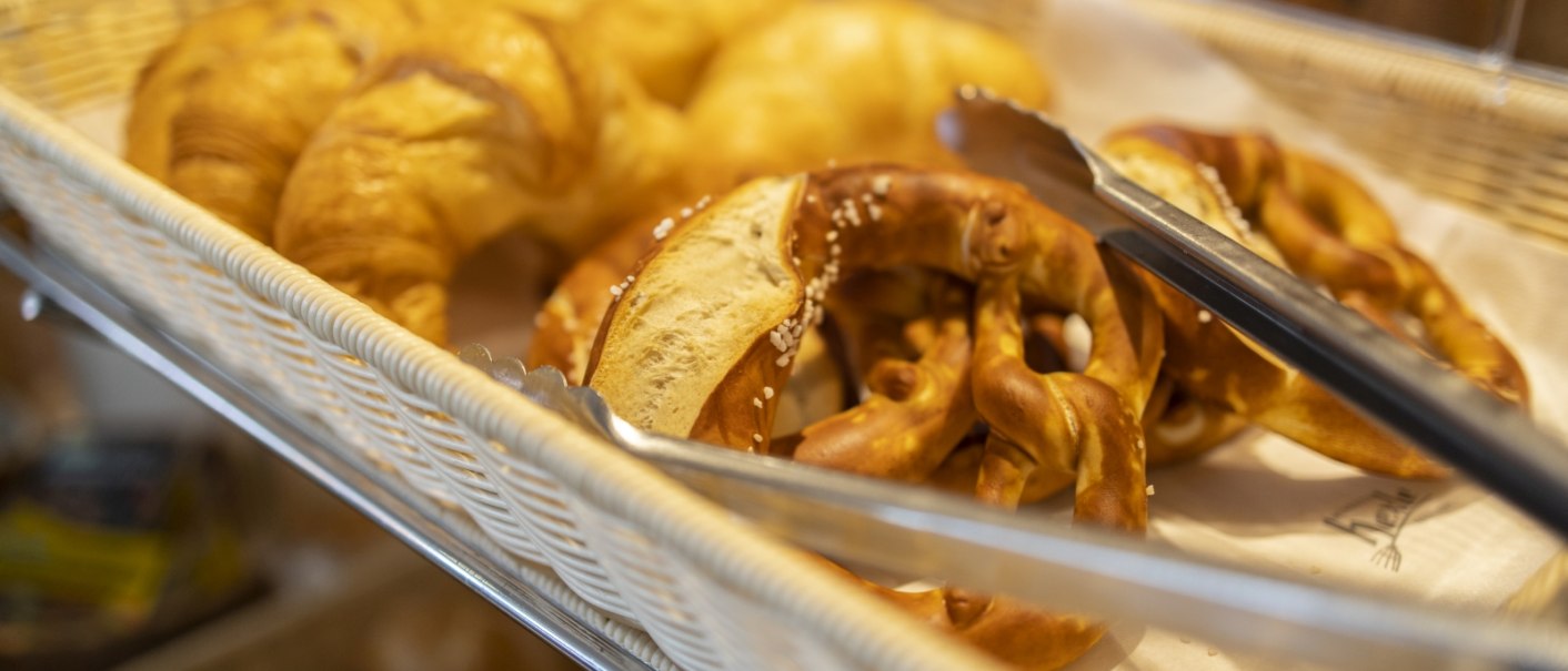 Ein Korb mit frischen Croissants und Brezeln, daneben liegt eine Zange zum Servieren., © Hotel Gloria GmbH Restaurant Möhringer Hexle Ein Korb mit frischen Croissants und Brezeln, daneben liegt eine Zange zum Servieren., © Hotel Gloria GmbH Restaurant Möhringer Hexle