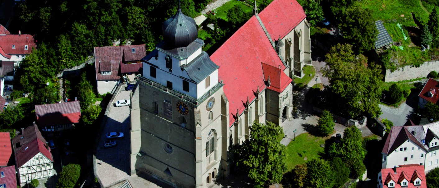 Luftaufnahme der Stiftskirche Herrenberg mit markantem Turm und rotem Dach, umgeben von Bäumen und Gebäuden., © Stuttgart-Marketing GmbH
