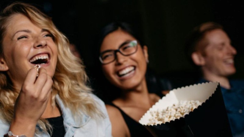 Drei Personen lachen und genießen Popcorn in einem Kino. Die Stimmung ist fröhlich und entspannt. Drei Personen lachen und genießen Popcorn in einem Kino. Die Stimmung ist fröhlich und entspannt.