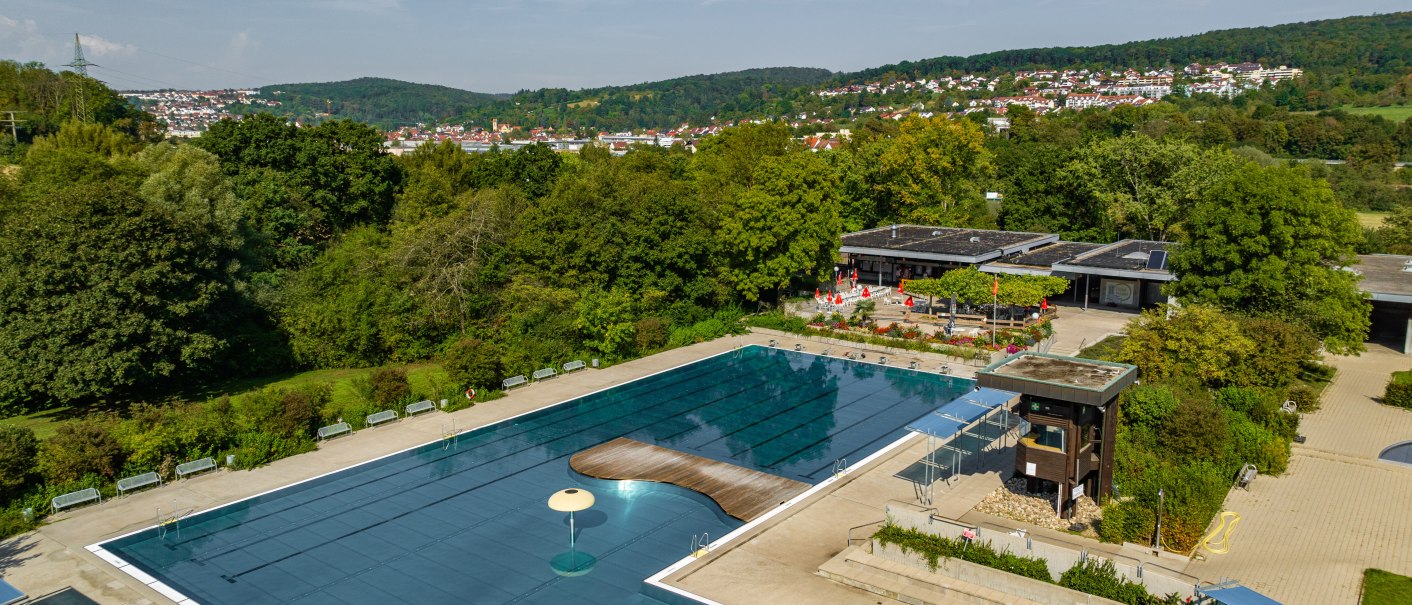 Luftaufnahme des Reichenbacher Freibads, umgeben von gr&uuml;nen B&auml;umen und H&uuml;geln. Ein gro&szlig;es Schwimmbecken und Geb&auml;ude sind sichtbar., &copy; Gemeinde Reichenbach a.d. Fils, Ingo Rack