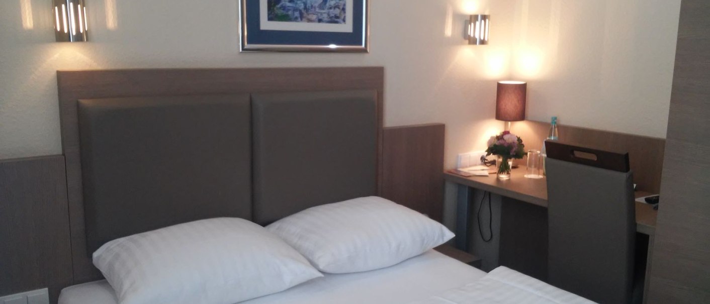 Ein gemütliches Hotelzimmer mit Queensize-Bett, Schreibtisch, Wandlampen und einem Bild an der Wand., © Novum Boulevard Stuttgart City