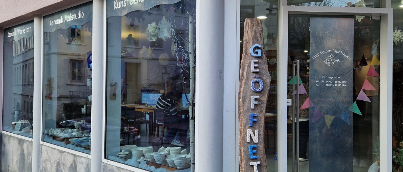 Au&szlig;enansicht eines Keramikstudios mit gro&szlig;en Fenstern. Ein Schild mit 'Ge&ouml;ffnet' steht vor der T&uuml;r. Innen sind Keramiken und Dekorationen sichtbar., &copy; StadtN&uuml;rtingen