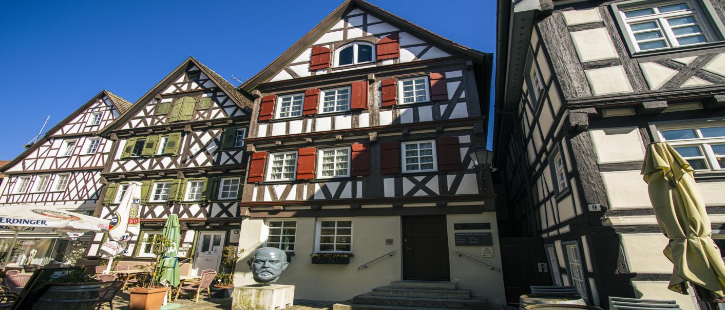 Fachwerkhäuser in Schorndorf bei sonnigem Wetter. Eine Büste steht vor einem der Häuser. Klare blaue Himmel im Hintergrund., © SMG Stuttgart Marketing GmbH - Sarah Schmid