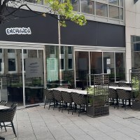 Außenbereich eines Restaurants namens Enchilada mit leeren Tischen und Stühlen. Ein Baum und Pflanzen trennen die Sitzbereiche., © SMG Außenbereich eines Restaurants namens Enchilada mit leeren Tischen und Stühlen. Ein Baum und Pflanzen trennen die Sitzbereiche., © SMG