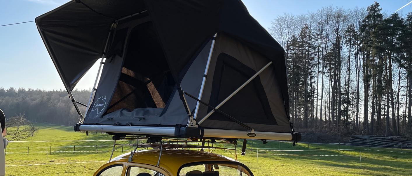 Ein Dachzelt ist auf einem gelben Auto montiert, im Hintergrund sind Bäume und ein blauer Himmel zu sehen., © seezeit GmbH Ein Dachzelt ist auf einem gelben Auto montiert, im Hintergrund sind Bäume und ein blauer Himmel zu sehen., © seezeit GmbH