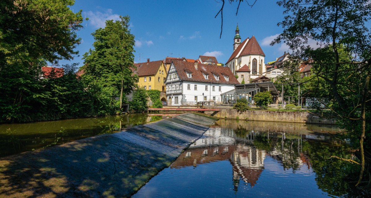 Die Rems in Waiblingen mit Fachwerkh&auml;usern und einer Kirche im Hintergrund, umgeben von B&auml;umen und blauem Himmel., &copy; Remstal Tourismus e.V.