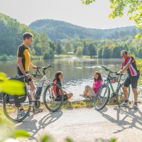 Vier Personen mit Fahrrädern genießen die Natur an einem Seeufer, umgeben von grüner Landschaft und Hügeln., © Landratsamt Rems-Murr-Kreis Vier Personen mit Fahrrädern genießen die Natur an einem Seeufer, umgeben von grüner Landschaft und Hügeln., © Landratsamt Rems-Murr-Kreis