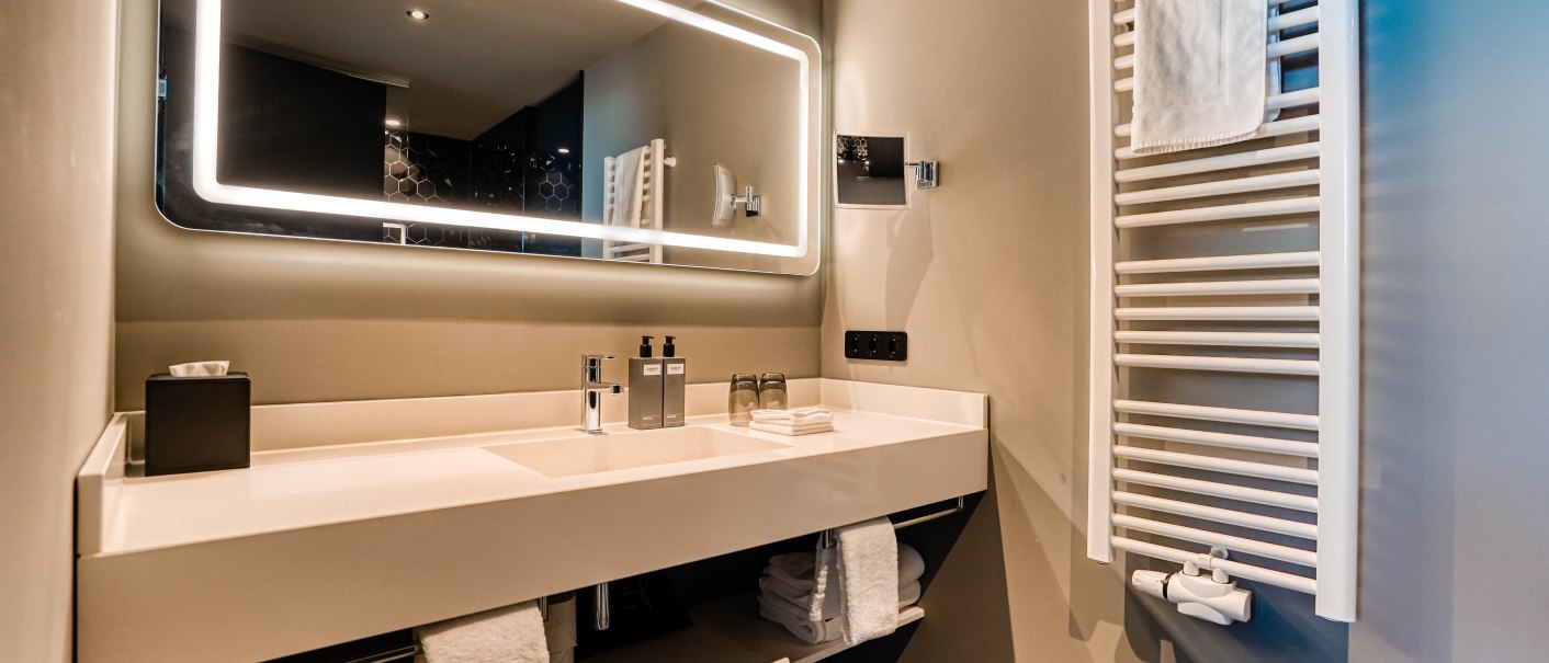 Modernes Badezimmer mit beleuchtetem Spiegel, Waschbecken und Handtuchhalter. Elegantes Design mit klaren Linien und neutralen Farben., © CLOUD N°7 APARTMENTS GmbH