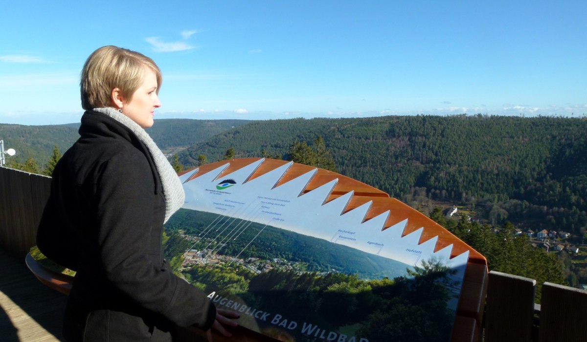 Frau an einem Aussichtspunkt im Naturpark Bad Wildbad, blickt auf bewaldete Hügel und ein Tal. Ein Informationsschild zeigt die Umgebung., © Naturpark Schwarzwald Mitte/Nord e.V. im Haus des Gastes Frau an einem Aussichtspunkt im Naturpark Bad Wildbad, blickt auf bewaldete Hügel und ein Tal. Ein Informationsschild zeigt die Umgebung., © Naturpark Schwarzwald Mitte/Nord e.V. im Haus des Gastes