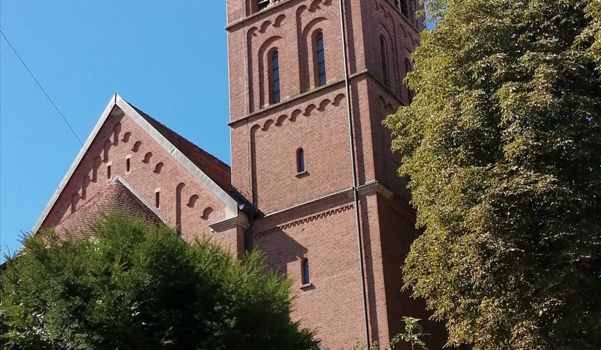 Die katholische Kirche St. Jakobus in Bargau mit ihrem markanten roten Backsteinturm und einer Uhr, umgeben von grünen Bäumen und strahlend blauem Himmel., © Foto: Cornelia Steinbach Die katholische Kirche St. Jakobus in Bargau mit ihrem markanten roten Backsteinturm und einer Uhr, umgeben von grünen Bäumen und strahlend blauem Himmel., © Foto: Cornelia Steinbach