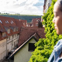 Blick von einer Stadtmauer auf rote Ziegeldächer und Weinberge im Hintergrund. Eine unscharfe Person ist im Vordergrund zu sehen., © SMG, Martina Denker