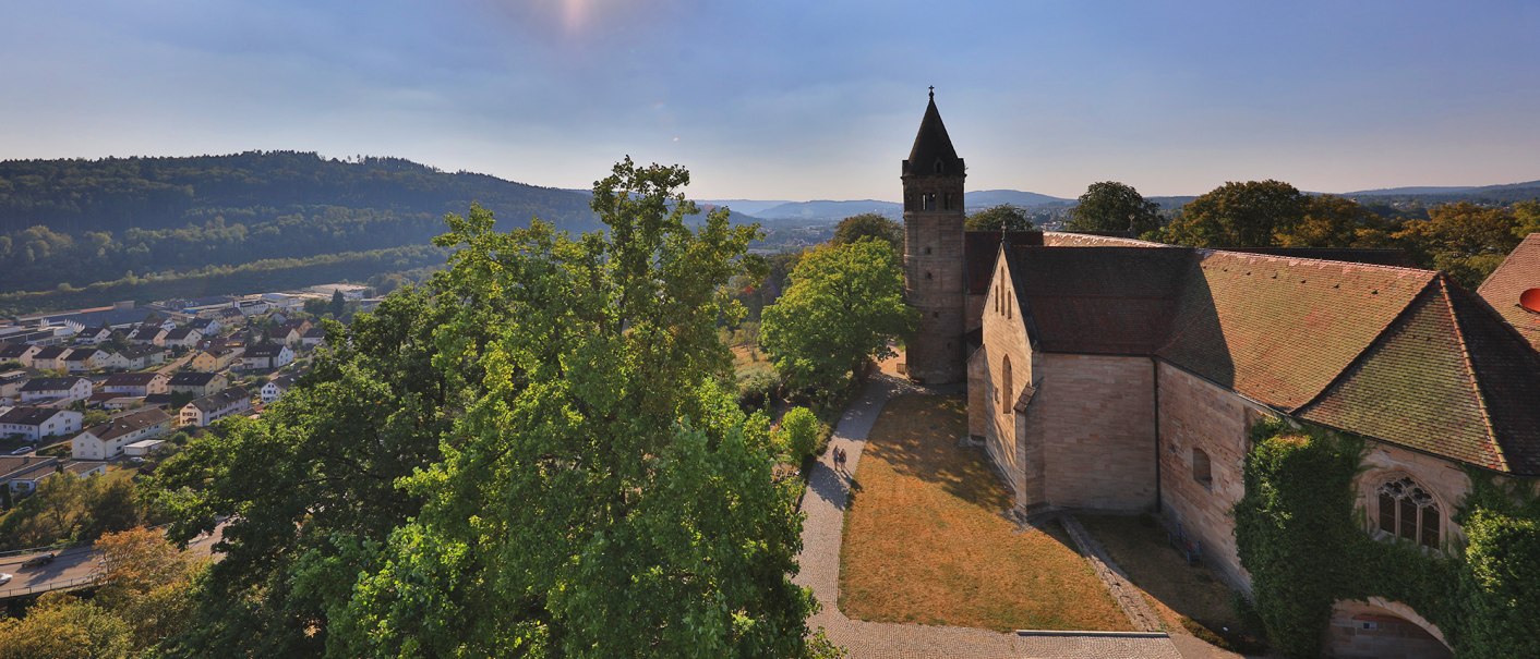 Kloster Lorch im Sonnenschein, umgeben von Bäumen und Hügeln. Im Hintergrund eine Stadt und bewaldete Hügel., © Stuttgart-Marketing GmbH, Achim Mende