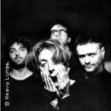 Schwarz-wei&szlig; Bild einer vierk&ouml;pfigen Band. Ein Mitglied steht im Vordergrund und h&auml;lt sein Gesicht mit den H&auml;nden. Die anderen sind unscharf im Hintergrund., &copy; links im Bild