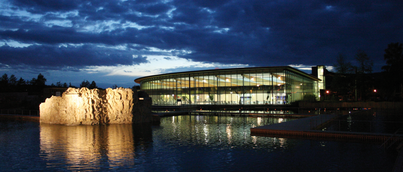Das Oskar Frech SeeBad bei Nacht, mit einem beleuchteten Felsen im Wasser und einem modernen, verglasten Geb&auml;ude im Hintergrund., &copy; SMG