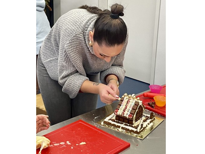 Eine Person dekoriert ein Lebkuchenhaus mit Zuckerguss und Süßigkeiten. Der Tisch ist mit roten Schneidebrettern und Backutensilien bedeckt., © Alfred Ritter GmbH & Co. KG | Waldenbuch Eine Person dekoriert ein Lebkuchenhaus mit Zuckerguss und Süßigkeiten. Der Tisch ist mit roten Schneidebrettern und Backutensilien bedeckt., © Alfred Ritter GmbH & Co. KG | Waldenbuch
