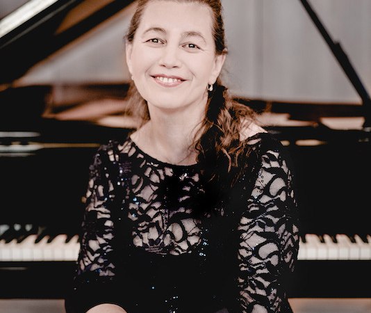 Eine Frau in einem eleganten schwarzen Spitzenkleid sitzt lächelnd vor einem Flügel., © Stadt Böblingen - Amt für Kultur