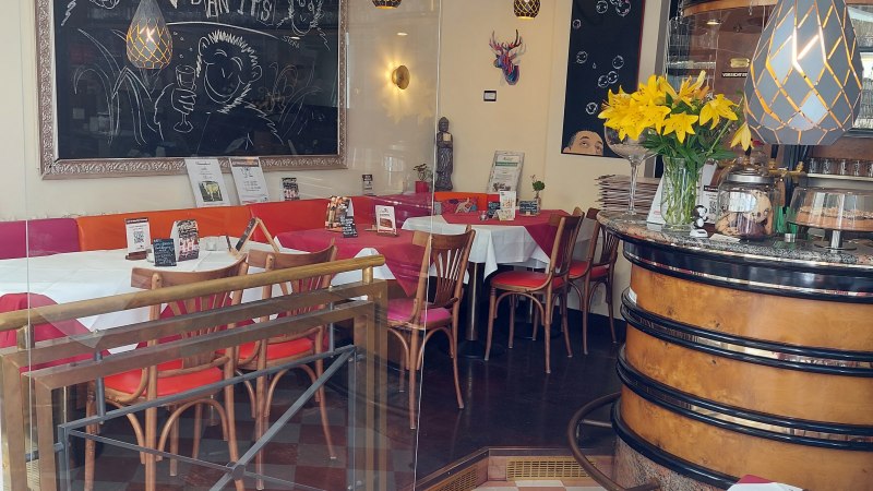 Ein gemütliches Restaurant mit Tafeln, gelben Blumen und gedeckten Tischen. Der Schriftzug 'V Bandits' ist auf einer Tafel zu sehen., © Lisa Bakavos V-Bandits Ein gemütliches Restaurant mit Tafeln, gelben Blumen und gedeckten Tischen. Der Schriftzug 'V Bandits' ist auf einer Tafel zu sehen., © Lisa Bakavos V-Bandits