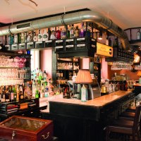 Bar mit Flaschen, Gläsern und Kupferdestille. Klosterfrau-Logo leuchtet im Hintergrund. Gemütliche Atmosphäre mit Holzmöbeln und Lampen., © Buschwerk Mediendesign-Wilhelmer Gastronomie