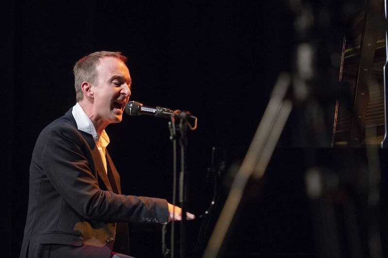 Ein Mann singt leidenschaftlich am Klavier auf einer B&uuml;hne. Er tr&auml;gt einen dunklen Anzug und ist in ein Mikrofon vertieft., &copy; Interessengemeinschaft Kultur Sindelfingen / B&ouml;blingen e.V.