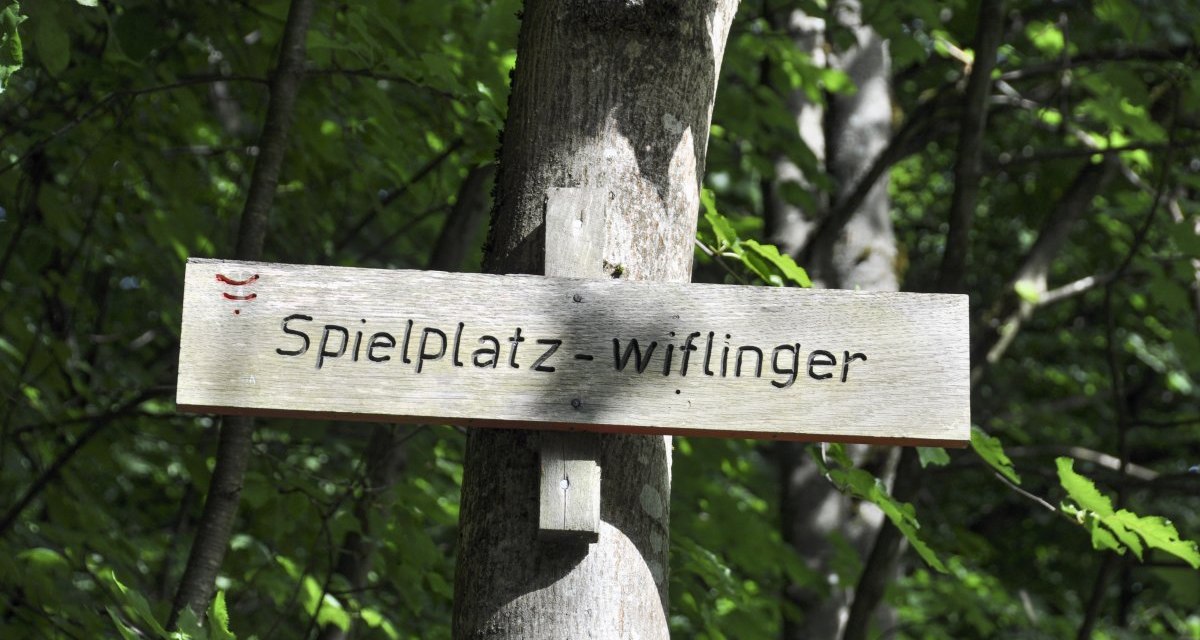 Ein Holzschild mit der Aufschrift 'Spielplatz - wiflinger' ist an einem Baum im Wald befestigt. Ein Holzschild mit der Aufschrift 'Spielplatz - wiflinger' ist an einem Baum im Wald befestigt.