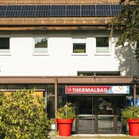 Eingang des Thermalbads in Bad Überkingen, umgeben von Pflanzen. Auf dem Dach sind Solarpanele installiert. Ein roter Blumentopf steht vor dem Eingang., © Stuttgart-Marketing GmbH, Sarah Schmid