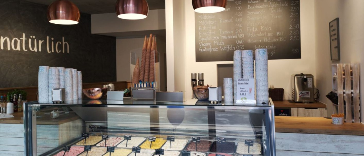 Eisdiele mit Eistheke, verschiedenen Eissorten, Menütafel und moderner Beleuchtung. Schriftzug 'natürlich' an der Wand., © Joannis Nakos Eisdiele mit Eistheke, verschiedenen Eissorten, Menütafel und moderner Beleuchtung. Schriftzug 'natürlich' an der Wand., © Joannis Nakos