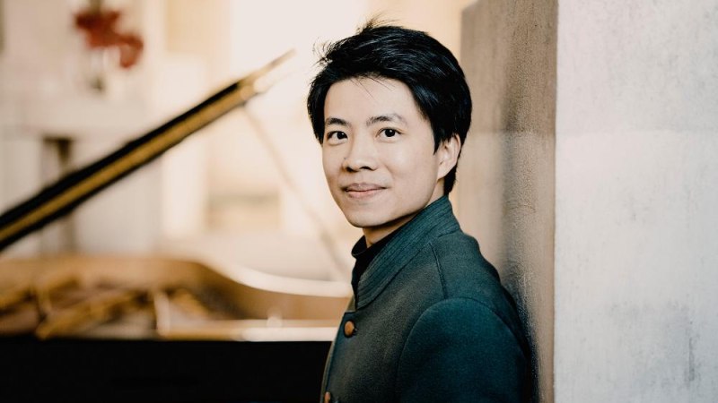 Eine Person lehnt l&auml;chelnd an einer Wand, im Hintergrund steht ein Fl&uuml;gel. Die Szene wirkt ruhig und einladend., &copy; Kit Armstrong &copy; Marco Borggreve