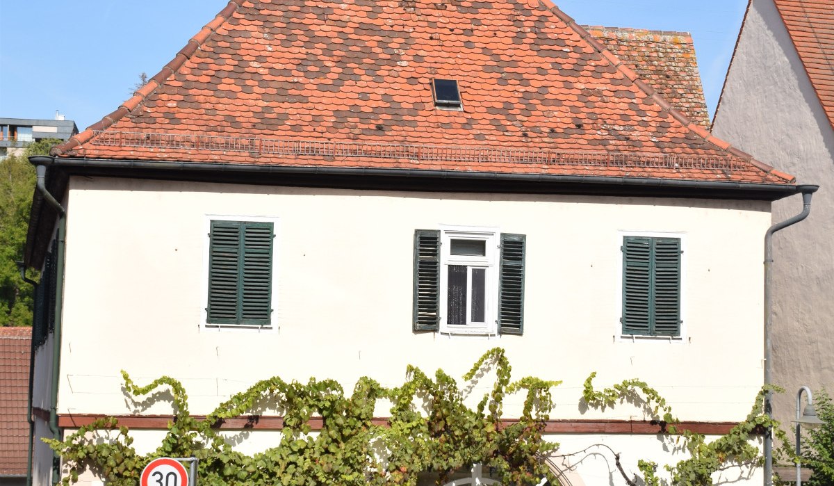 Zweigeschossiges Gebäude mit rotem Ziegeldach, grünen Fensterläden und Weinreben. Drei Autos parken davor, Verkehrsschild zeigt 30 km/h., © Land der 1000 Hügel - Kraichgau-Stromberg Zweigeschossiges Gebäude mit rotem Ziegeldach, grünen Fensterläden und Weinreben. Drei Autos parken davor, Verkehrsschild zeigt 30 km/h., © Land der 1000 Hügel - Kraichgau-Stromberg