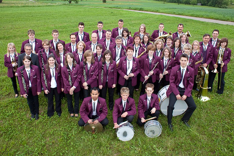 Eine gro&szlig;e Blaskapelle in lila Uniformen posiert auf einer gr&uuml;nen Wiese. Die Mitglieder halten verschiedene Blasinstrumente., &copy; Tobias Froehner