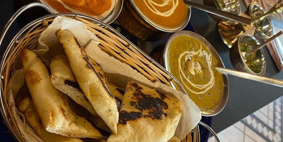 Drei Schalen mit indischen Currys und ein Korb mit Naan-Brot auf einem Tisch in einem Restaurant., © Taj Mahal Bad Urach