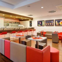 Moderne Bar mit roten und grauen M&ouml;beln, beleuchtetem Tresen und Wandbildern von Getr&auml;nken. Elegantes Ambiente mit Holzboden., &copy; Ibis Stuttgart Airport Messe