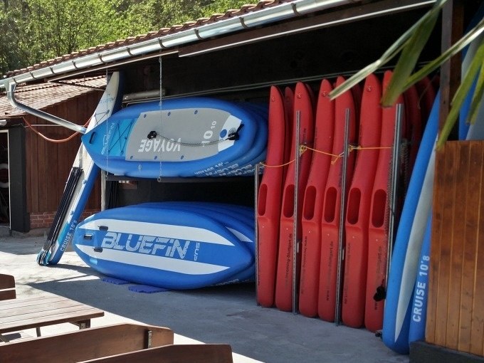 Gestapelte Stand-Up-Paddleboards in einem offenen Schuppen, umgeben von Holzwänden und einem Ziegeldach., © Cool-Tours StattReisen Gestapelte Stand-Up-Paddleboards in einem offenen Schuppen, umgeben von Holzwänden und einem Ziegeldach., © Cool-Tours StattReisen