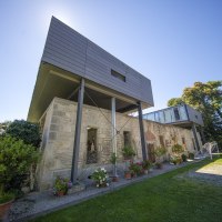 Modernes Gebäude mit alten Steinmauern und Glasstruktur, umgeben von Pflanzen und Bäumen unter blauem Himmel., © Region Stuttgart