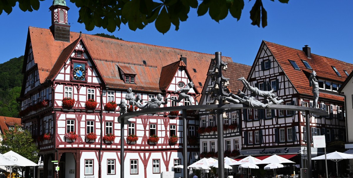 Fachwerkhäuser umgeben einen Marktplatz mit dem Schäferlauf-Denkmal. Im Vordergrund sind Tische und Sonnenschirme zu sehen., © Bad Urach Tourismus Fachwerkhäuser umgeben einen Marktplatz mit dem Schäferlauf-Denkmal. Im Vordergrund sind Tische und Sonnenschirme zu sehen., © Bad Urach Tourismus