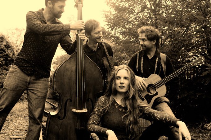 Ein Jazz-Quartett posiert im Freien. Eine Frau sitzt, während drei Männer mit Kontrabass und Gitarre um sie herumstehen. Sepia-Ton., © Stadt Murrhardt