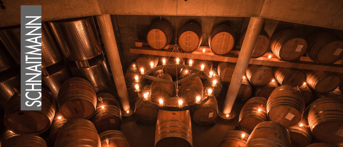 Weinkeller mit Holzf&auml;ssern, warmem Licht und Kronleuchter; links das Logo &bdquo;SCHINATMANN&ldquo;., &copy; Weingut Schnaitmann