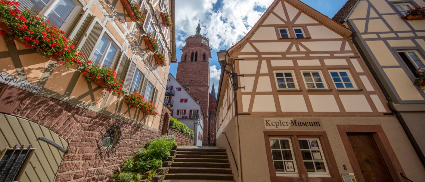 Fachwerkhäuser in der Keplergasse, Weil der Stadt. Das Keplermuseum ist sichtbar, mit einem Kirchturm im Hintergrund und blühenden Blumen an den Fenstern., © SMG, Achim Mende