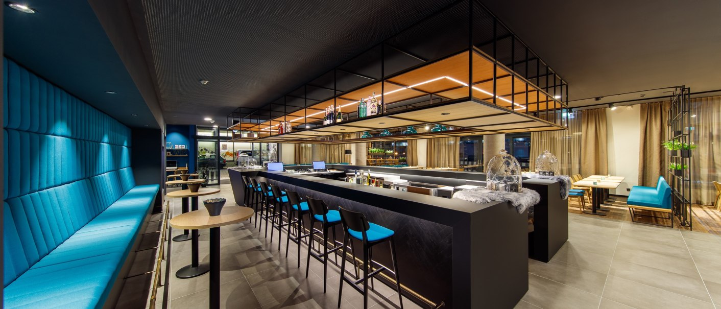 Moderne Bar mit blauen Sitzbänken und Hockern, stilvolle Beleuchtung und dekorative Elemente. Elegantes, minimalistisches Design., © Arthotel ANA Momentum Moderne Bar mit blauen Sitzbänken und Hockern, stilvolle Beleuchtung und dekorative Elemente. Elegantes, minimalistisches Design., © Arthotel ANA Momentum