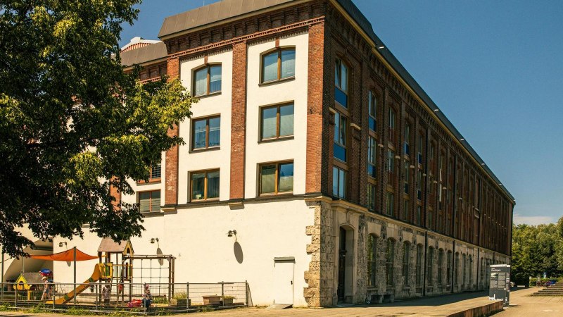 Ein altes Backsteingebäude mit modernen Fenstern, daneben ein Spielplatz mit bunten Sonnensegeln. Bäume im Vordergrund und blauer Himmel., © Stuttgart-Marketing GmbH, Sarah Schmid Ein altes Backsteingebäude mit modernen Fenstern, daneben ein Spielplatz mit bunten Sonnensegeln. Bäume im Vordergrund und blauer Himmel., © Stuttgart-Marketing GmbH, Sarah Schmid