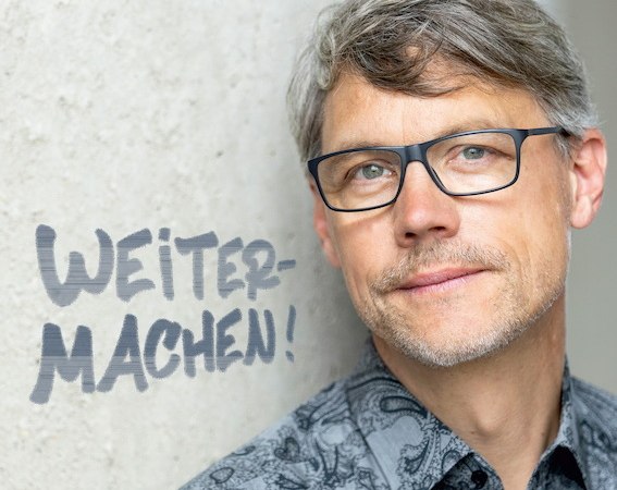 Ein Mann mit Brille und gemustertem Hemd lehnt an einer Wand. Daneben steht der Schriftzug 'WEITERMACHEN!' in Großbuchstaben., © Naturfreunde Schorndorf e.V.