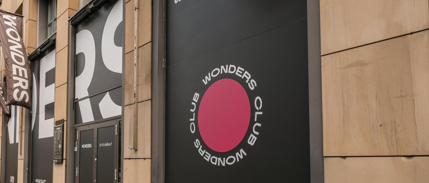 Eingang des Wonders Club mit großem Logo und Schriftzug an der Fassade. Schwarze Türen und ein pinker Kreis mit dem Text 'Wonders Club'., © Stuttgart Marketing GmbH, Sarah Schmid