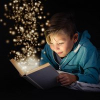 Ein Kind in einem blauen Hoodie liest ein Buch, aus dem funkelnde Lichter aufsteigen, vor schwarzem Hintergrund., &copy; Stadt N&uuml;rtingen