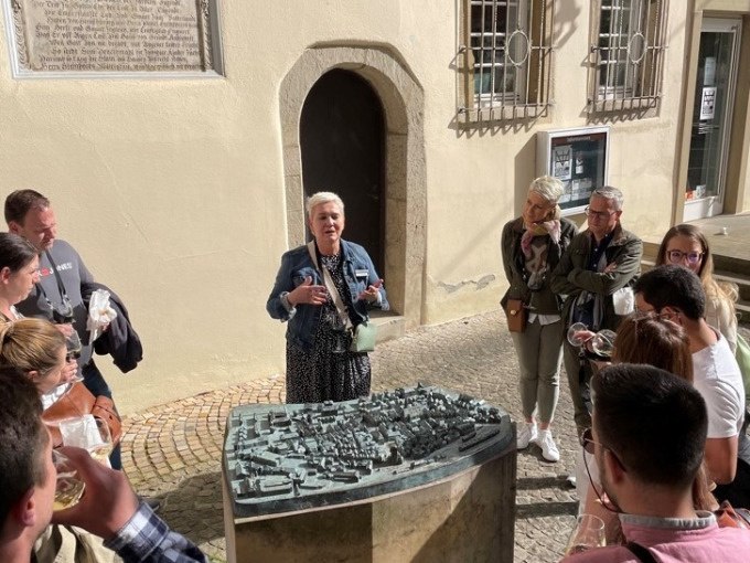 Eine Frau hält eine Führung vor einem Stadtmodell im Freien, umgeben von einer Gruppe interessierter Zuhörer., © Eigenbetrieb Tourismus und Citymanagement Schorndorf