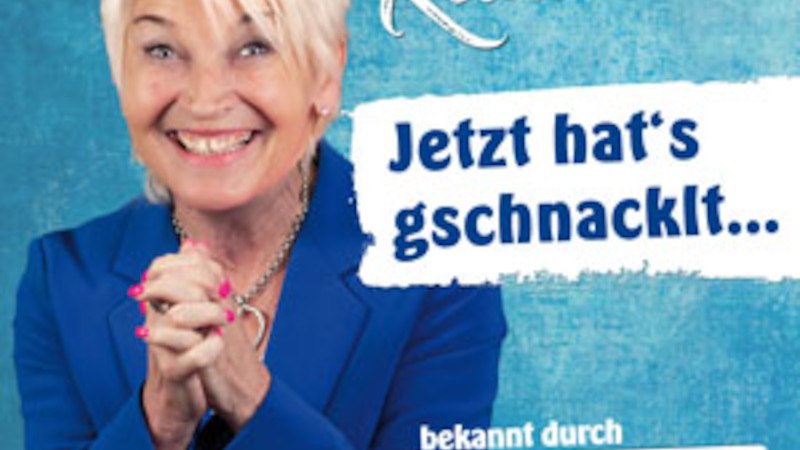 Frau in blauem Blazer lächelt vor blauem Hintergrund. Text: "Jetzt hat's gschnacklt..." und "bekannt durch Dui do on de Sell"., © C² CONCERTS GmbH