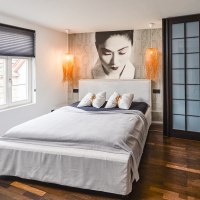 Modernes Hotelzimmer mit großem Bett, Wandbild einer Frau, zwei Hängelampen und Holzfußboden., © Zauberlehrling Modernes Hotelzimmer mit großem Bett, Wandbild einer Frau, zwei Hängelampen und Holzfußboden., © Zauberlehrling