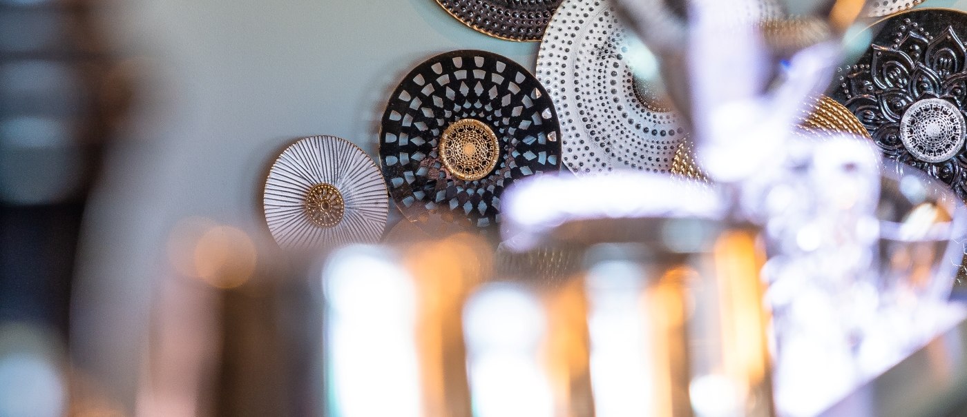 Dekorative Teller in Gold, Schwarz und Weiß an einer Wand. Unscharfe Barutensilien im Vordergrund., © MASEVEN Stuttgart SI-Centrum Dekorative Teller in Gold, Schwarz und Weiß an einer Wand. Unscharfe Barutensilien im Vordergrund., © MASEVEN Stuttgart SI-Centrum