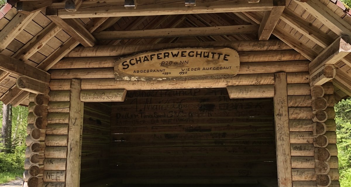 Eine rustikale Holzhütte im Wald, genannt 'Schäferweghütte', mit einem Schild über dem Eingang. Umgeben von hohen Bäumen., © Nördlicher Schwarzwald Eine rustikale Holzhütte im Wald, genannt 'Schäferweghütte', mit einem Schild über dem Eingang. Umgeben von hohen Bäumen., © Nördlicher Schwarzwald