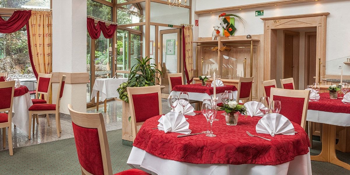 Elegantes Restaurant mit roten Tischdecken, Holzstühlen und großen Fenstern. Tische sind mit Gläsern und Servietten gedeckt, Pflanzen dekorieren den Raum., © Hotel Restaurant Lamm